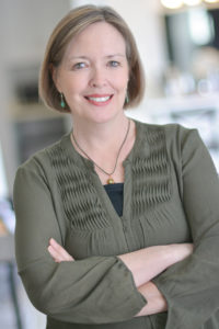 Image of a woman wearing an olive green three quarter sleeve blouse with her arms crossed in front of her body.