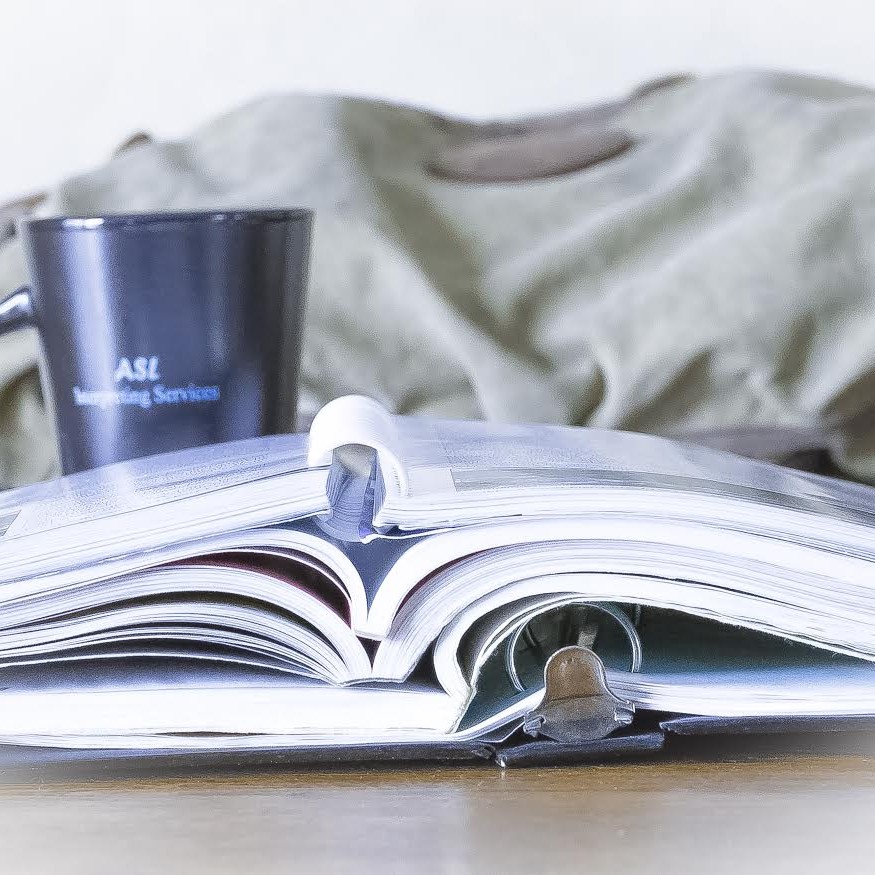 Image of a binder and books sitting on a table with an ASL Interpreting mug sitting behind them.