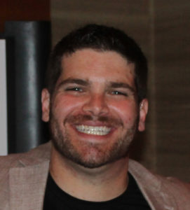 Image of Corey Axelrod wearing a tan blazer and black shirt smiling at the camera.
