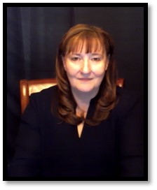 Image of Charlene Crump sitting on a brown chair smiling at the camera.