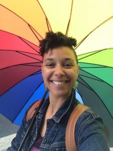 Image of Amy Parsons holding a rainbow umbrella smiling. 