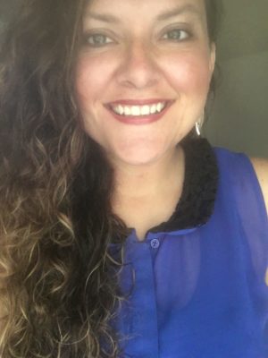 Image of Bree Logan with long curly hair wearing a purple button up tank top and black collar.
