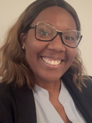 Tanesh, black female wearing dark glasses, a light grey blouse and black blazer.